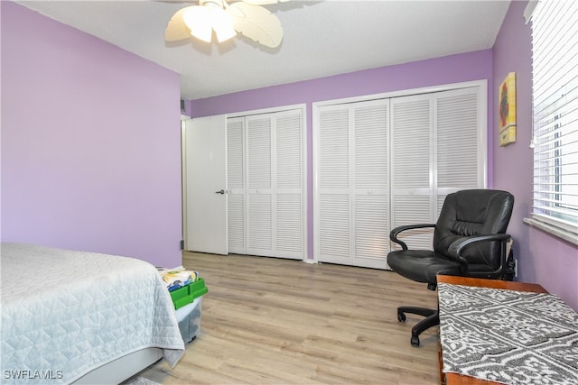 bedroom with ceiling fan, a textured ceiling, light wood-type flooring, and two closets