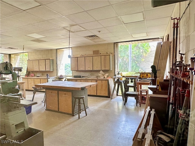 kitchen featuring light brown cabinets, tile countertops, a kitchen bar, a center island, and a paneled ceiling