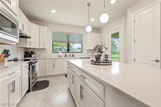 kitchen featuring light stone counters, white cabinets, appliances with stainless steel finishes, and decorative light fixtures