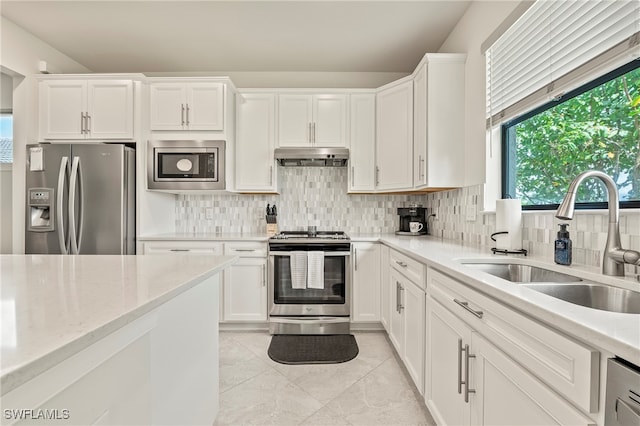 kitchen featuring appliances with stainless steel finishes, white cabinetry, tasteful backsplash, light tile patterned floors, and sink