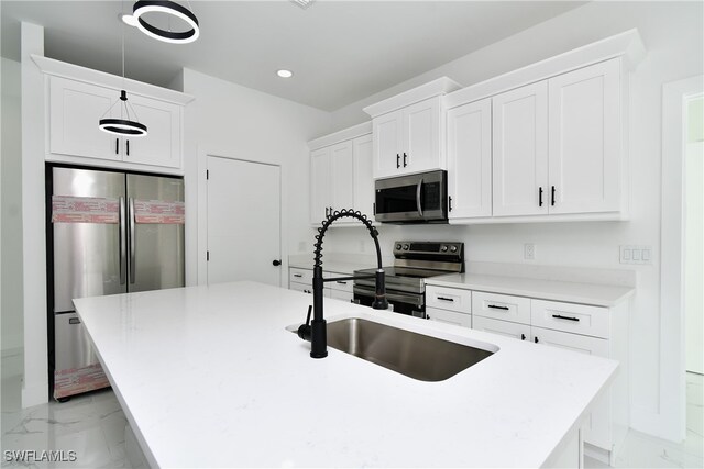 kitchen featuring white cabinetry, decorative light fixtures, stainless steel appliances, an island with sink, and sink