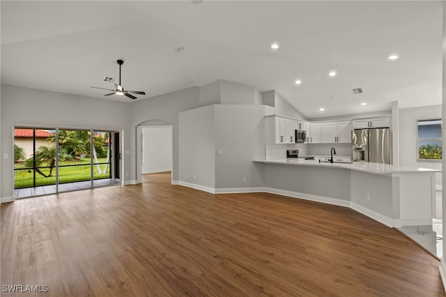 unfurnished living room featuring ceiling fan, sink, hardwood / wood-style floors, and vaulted ceiling