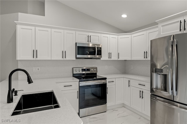 kitchen featuring vaulted ceiling, light stone countertops, stainless steel appliances, sink, and white cabinets