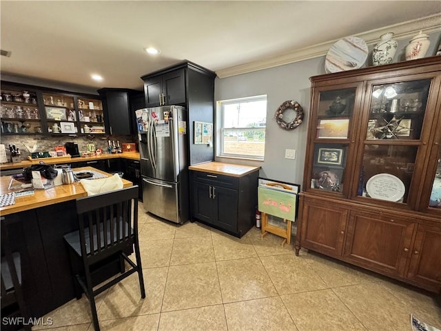 kitchen featuring crown molding, tasteful backsplash, stainless steel fridge with ice dispenser, light tile patterned floors, and wood counters