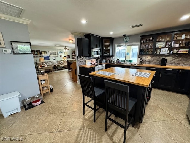 kitchen featuring a kitchen breakfast bar, butcher block counters, appliances with stainless steel finishes, and light tile patterned flooring