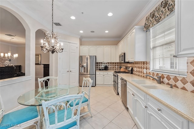 kitchen with hanging light fixtures, white cabinetry, stainless steel appliances, crown molding, and a chandelier