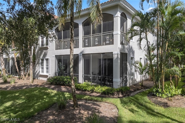 rear view of property with a balcony, a sunroom, and a yard