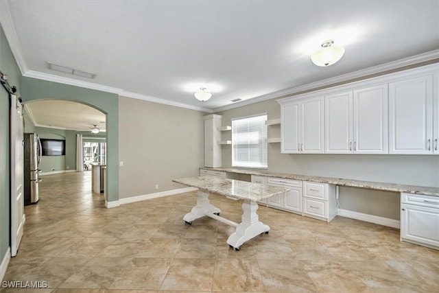 unfurnished office with crown molding, built in desk, ceiling fan, and a barn door