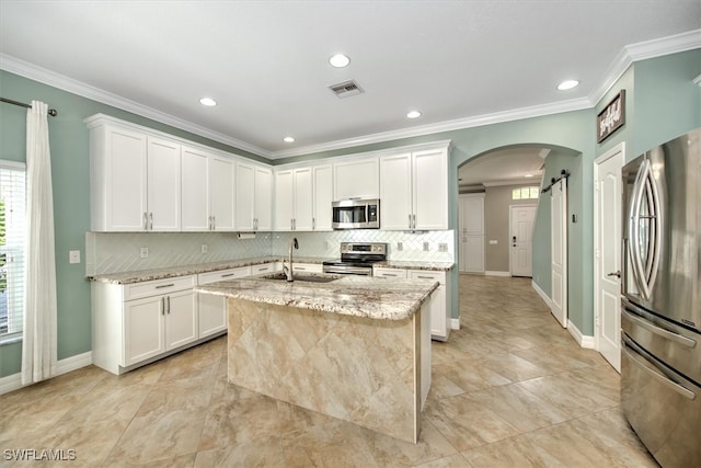 kitchen with a barn door, appliances with stainless steel finishes, light stone countertops, sink, and an island with sink