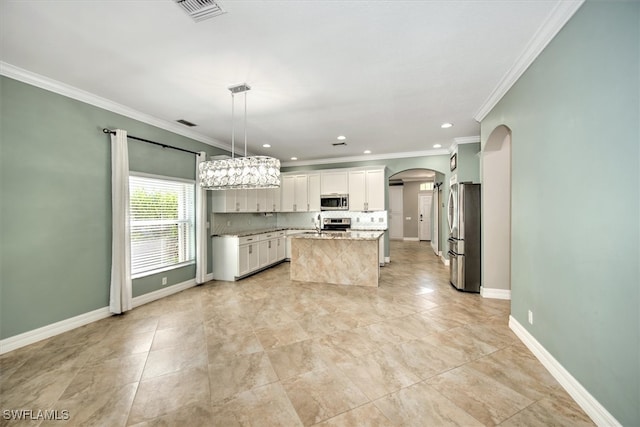 kitchen with white cabinets, a center island, appliances with stainless steel finishes, pendant lighting, and ornamental molding