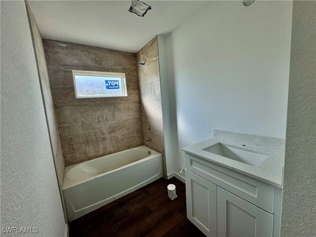 bathroom with a textured ceiling, vanity, hardwood / wood-style floors, and tiled shower / bath