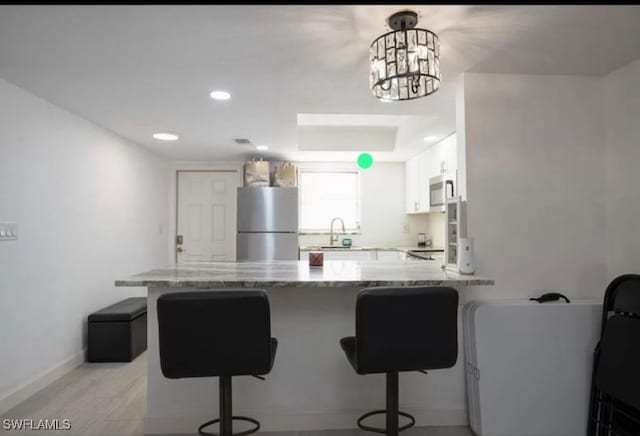 kitchen with stainless steel appliances, a kitchen bar, light stone countertops, white cabinets, and kitchen peninsula