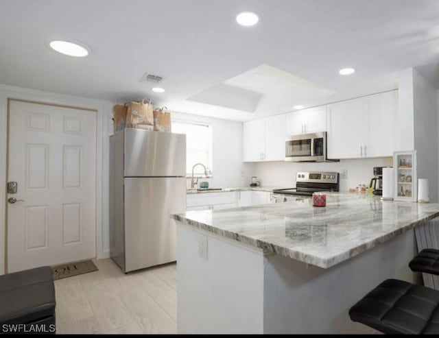 kitchen with stainless steel appliances, white cabinetry, kitchen peninsula, a kitchen breakfast bar, and light stone countertops