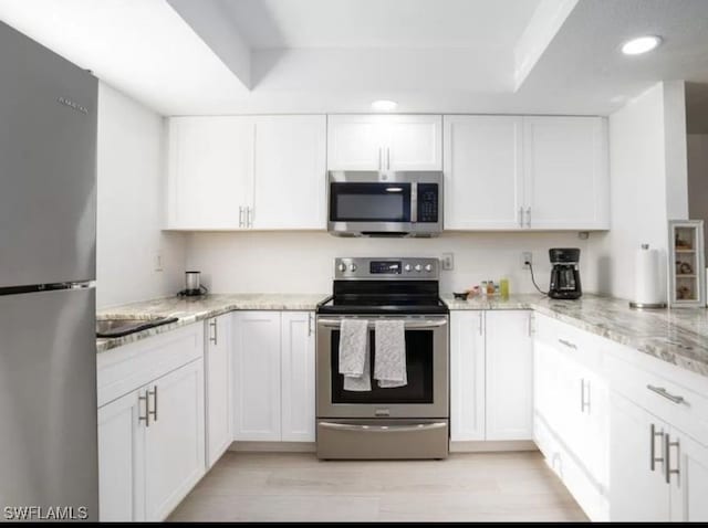 kitchen featuring light hardwood / wood-style floors, white cabinetry, appliances with stainless steel finishes, and light stone countertops