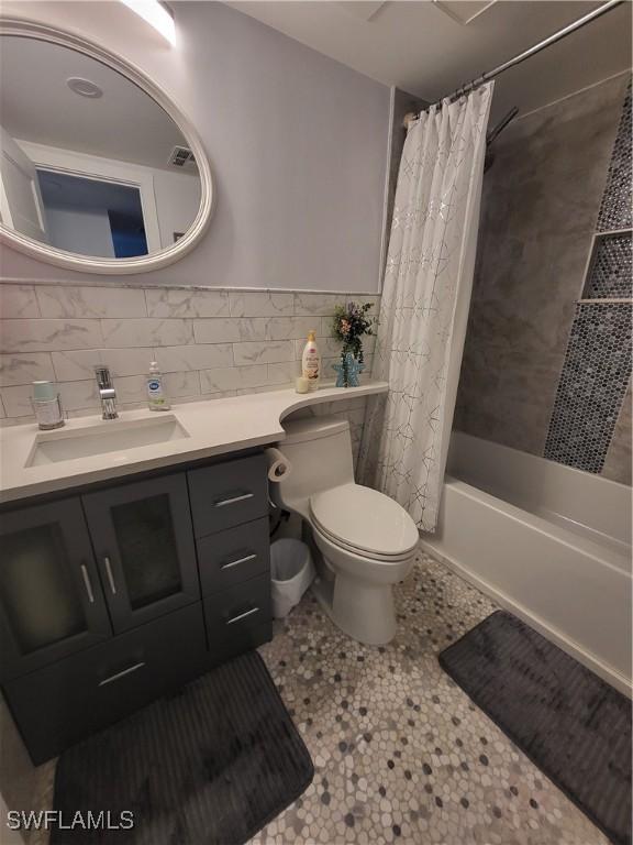 full bathroom featuring vanity, shower / bath combination with curtain, tile patterned flooring, toilet, and tile walls