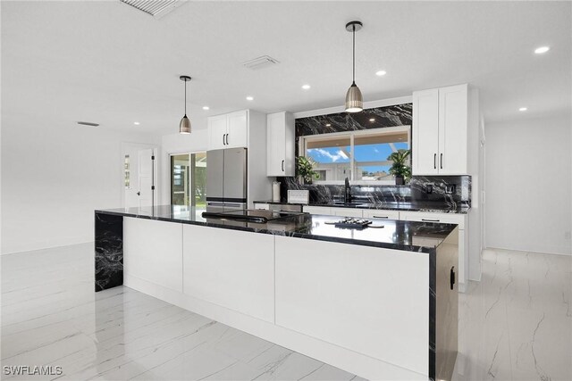 kitchen with stainless steel gas stovetop, decorative light fixtures, white cabinets, a center island, and fridge