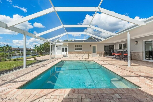 view of pool featuring glass enclosure, a patio area, and a water view