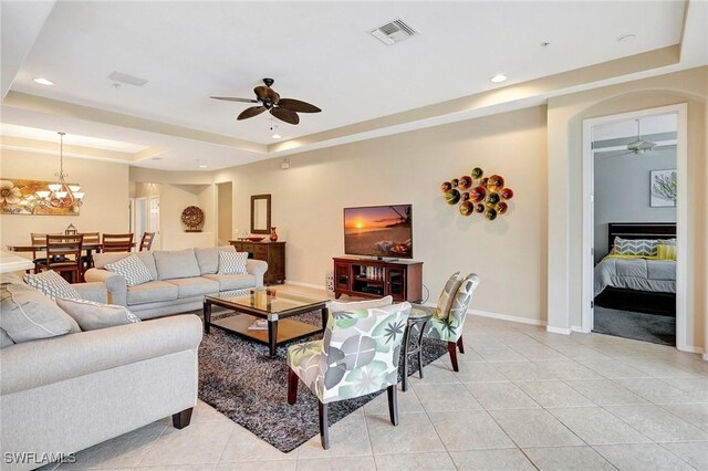 living room with ceiling fan with notable chandelier, a tray ceiling, and light tile patterned floors