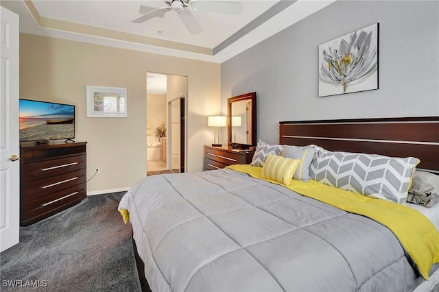 bedroom with baseboards, a raised ceiling, a ceiling fan, ensuite bath, and dark carpet