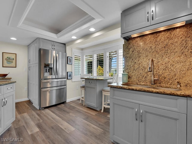 kitchen featuring a raised ceiling, tasteful backsplash, light wood-type flooring, and stainless steel refrigerator with ice dispenser