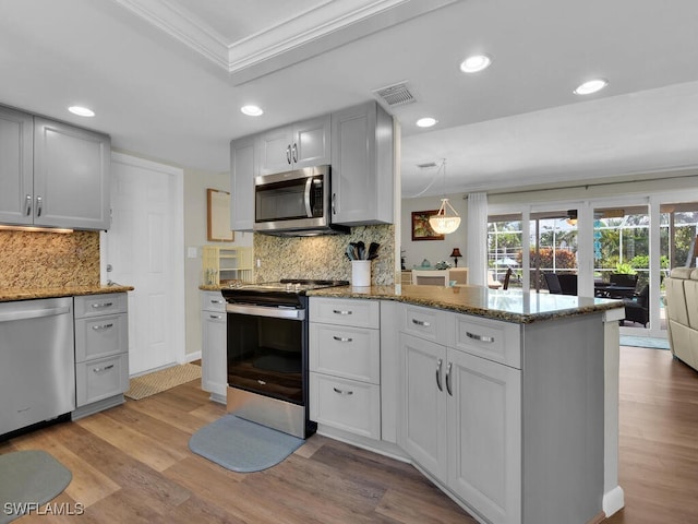 kitchen featuring kitchen peninsula, crown molding, light wood-type flooring, appliances with stainless steel finishes, and tasteful backsplash