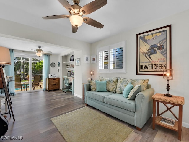 living room with built in shelves, ceiling fan, dark wood-type flooring, and a wealth of natural light