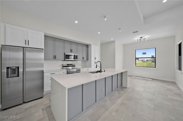 kitchen featuring an island with sink, sink, stainless steel appliances, and gray cabinetry