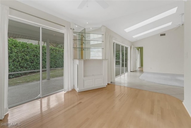 spare room featuring light hardwood / wood-style flooring, lofted ceiling with skylight, and ceiling fan