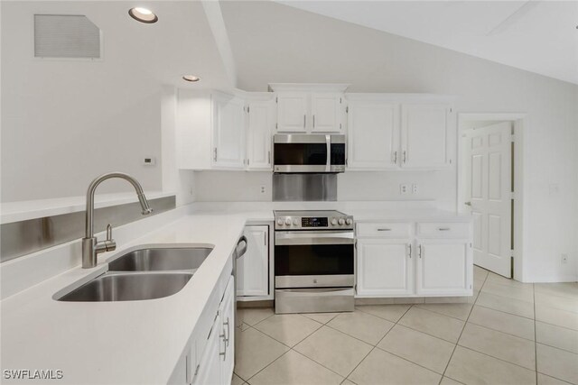 kitchen featuring lofted ceiling, sink, light tile patterned floors, appliances with stainless steel finishes, and white cabinetry