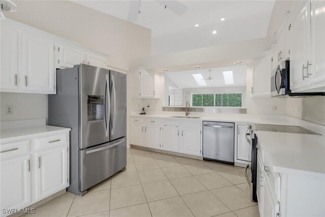 kitchen featuring stainless steel appliances, sink, vaulted ceiling with skylight, and white cabinets