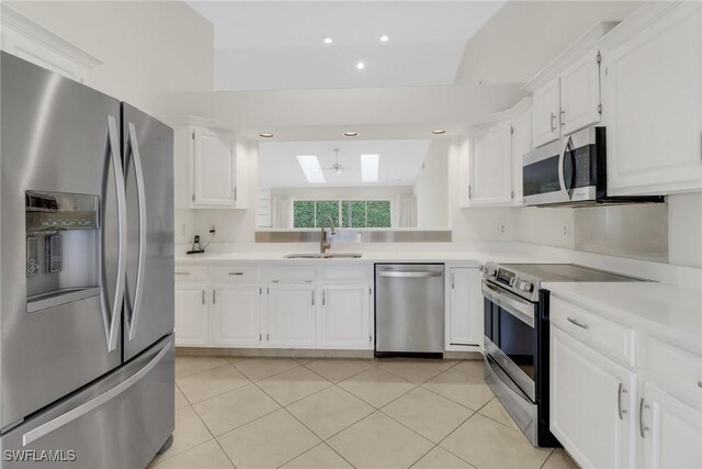 kitchen with sink, white cabinetry, a skylight, light tile patterned floors, and stainless steel appliances