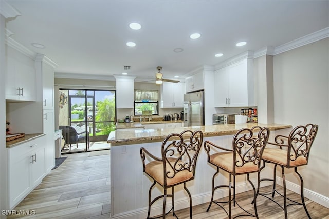 kitchen with light stone counters, white cabinetry, kitchen peninsula, ceiling fan, and stainless steel fridge with ice dispenser