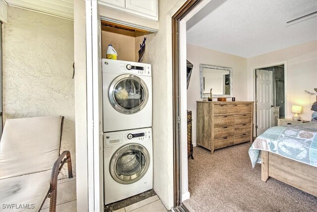 washroom with a textured ceiling, stacked washer and clothes dryer, and light colored carpet