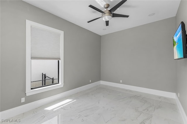 unfurnished room featuring a healthy amount of sunlight, marble finish floor, baseboards, and a ceiling fan