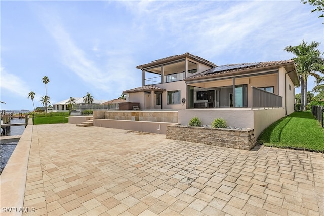 back of house featuring solar panels, fence, a tiled roof, and stucco siding