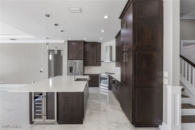 kitchen with stainless steel appliances, wall chimney range hood, light stone counters, a large island with sink, and decorative light fixtures