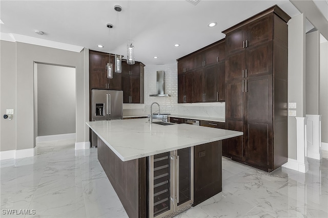 kitchen with pendant lighting, wall chimney exhaust hood, an island with sink, light stone counters, and beverage cooler