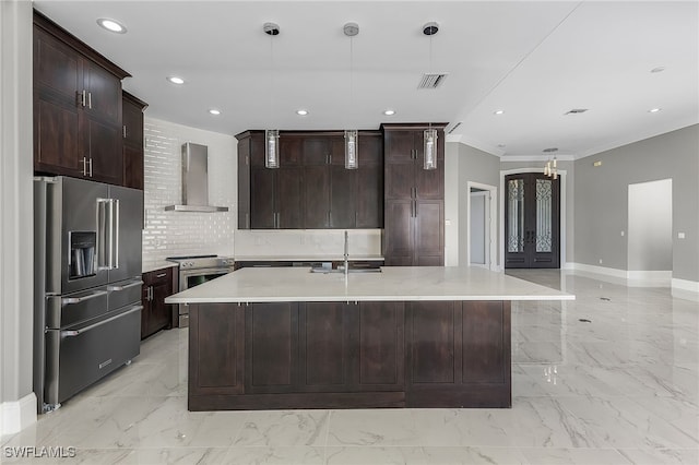 kitchen featuring sink, wall chimney exhaust hood, stainless steel appliances, decorative light fixtures, and a center island with sink