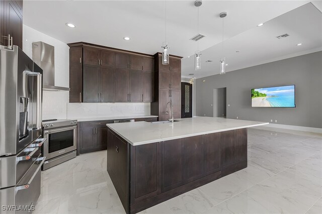 kitchen with appliances with stainless steel finishes, wall chimney exhaust hood, a kitchen island with sink, sink, and hanging light fixtures