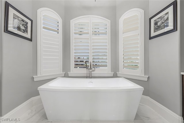 bathroom featuring marble finish floor, a freestanding tub, and baseboards