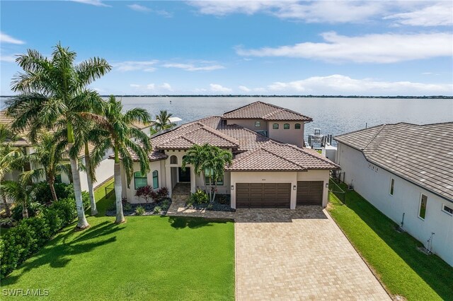 mediterranean / spanish house featuring a garage, a tile roof, decorative driveway, stucco siding, and a front lawn