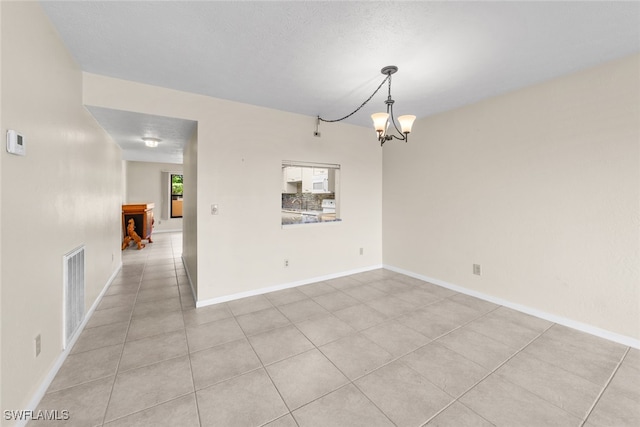 empty room featuring light tile patterned floors, a textured ceiling, and an inviting chandelier