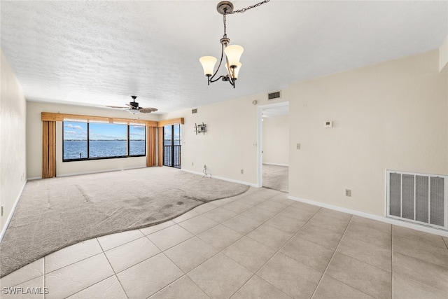 unfurnished living room with a textured ceiling, a water view, light colored carpet, and ceiling fan with notable chandelier