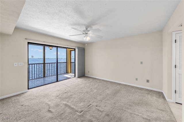 carpeted spare room with a textured ceiling, a water view, and ceiling fan