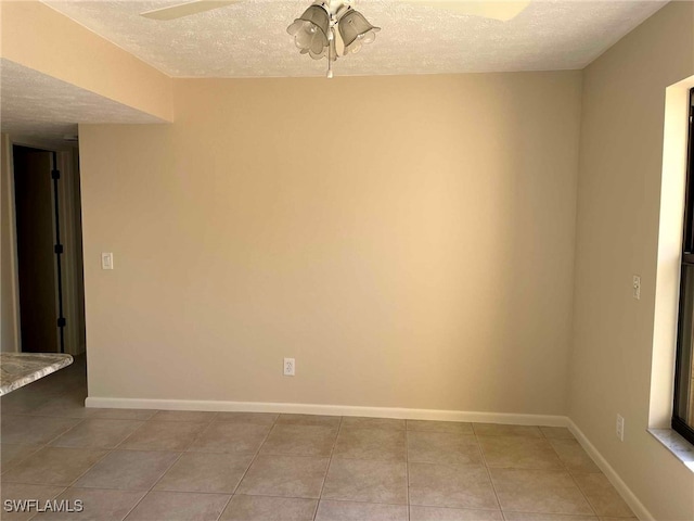 empty room with ceiling fan, a textured ceiling, baseboards, and light tile patterned floors