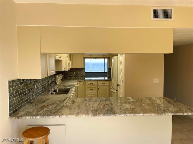 kitchen with white appliances, visible vents, decorative backsplash, a breakfast bar area, and a peninsula