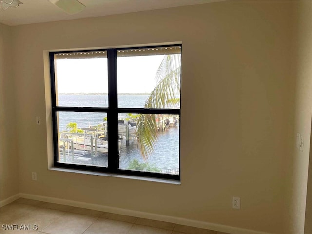 unfurnished room with a water view, light tile patterned floors, and baseboards