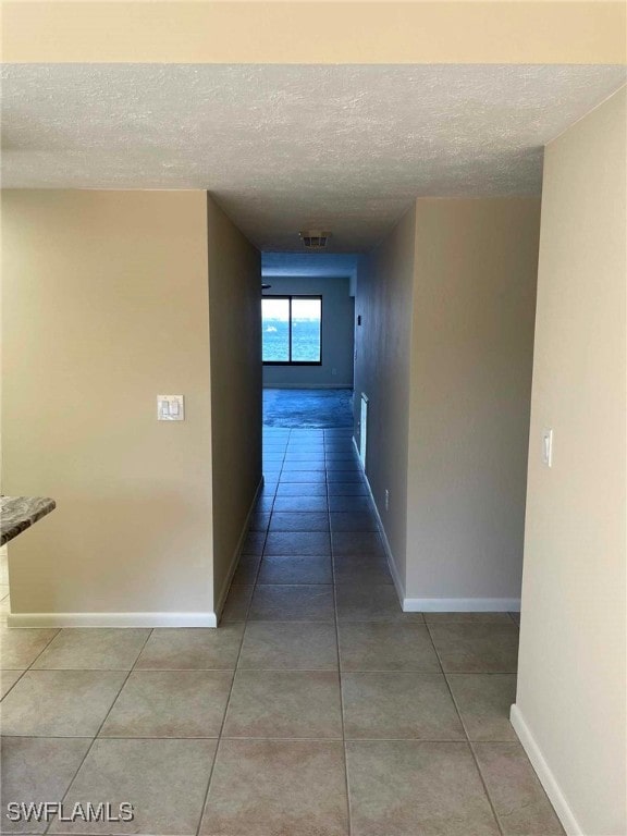 hall featuring tile patterned flooring, visible vents, baseboards, and a textured ceiling