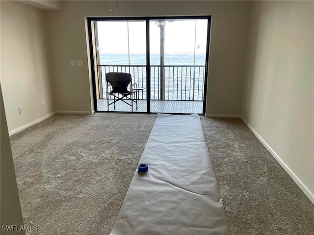 carpeted spare room featuring a water view and baseboards