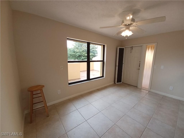 empty room with light tile patterned floors, a ceiling fan, and baseboards